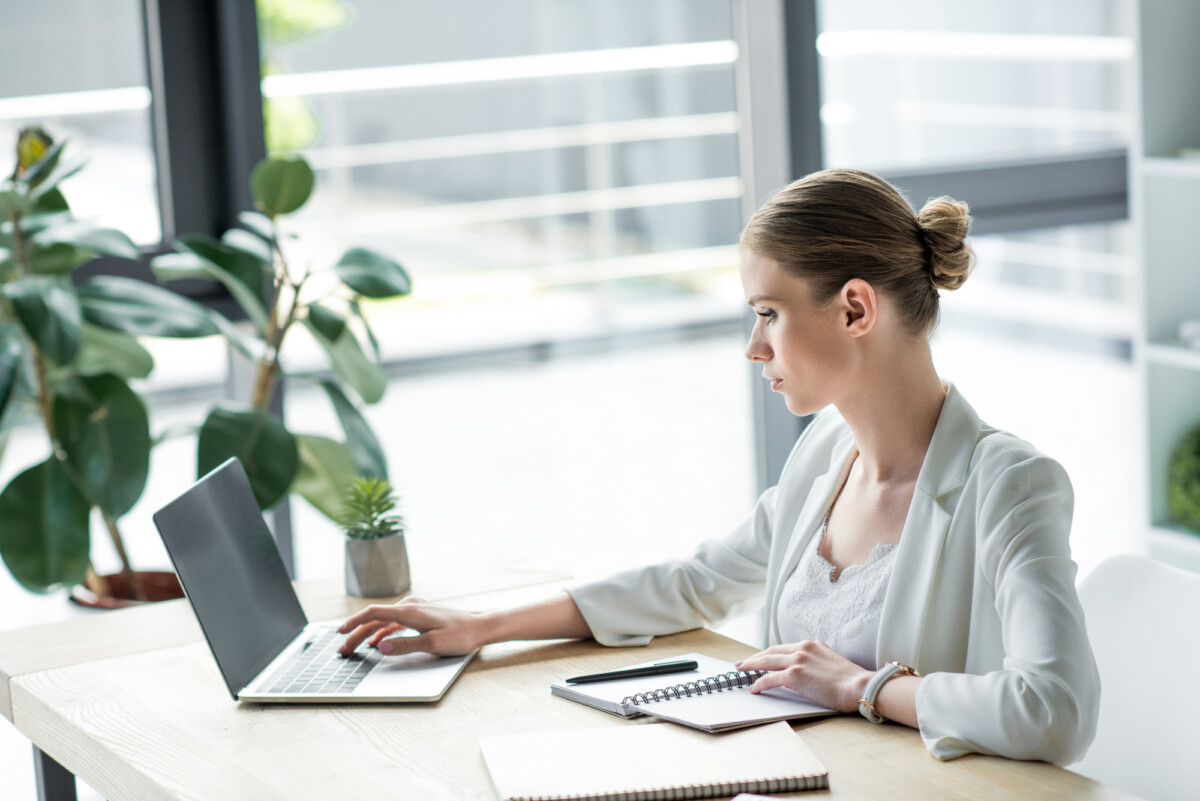 A focused professional woman working intently on a laptop at a bright and modern office desk.