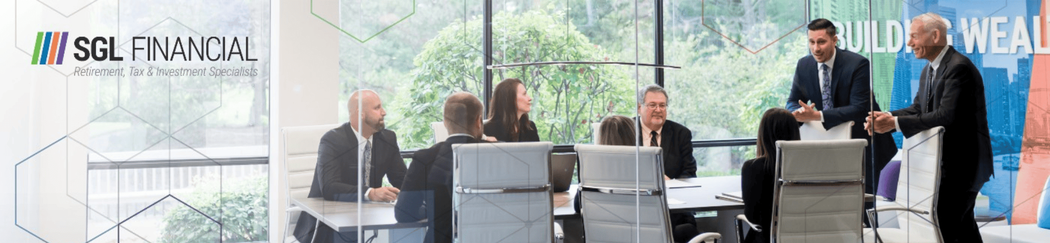 A group of business professionals is seated around a conference table in a modern office. Two men are standing and speaking to those seated. The room has large windows with a view of greenery outside. The SGL Financial logo and tagline are displayed on the left.