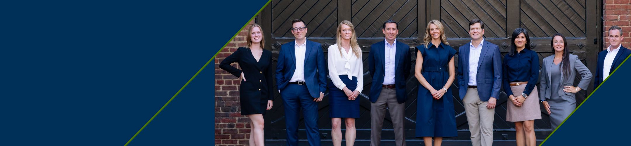 A group of nine professionals, dressed in business attire, stand in a row outdoors in front of a large wooden door and brick wall, smiling at the camera. Blue and green diagonal lines frame the left side.