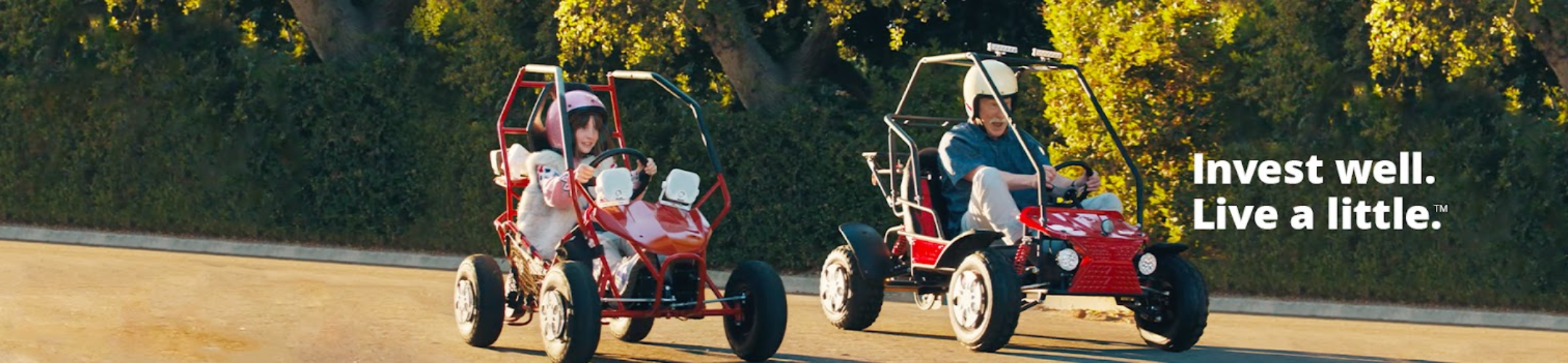 Two people ride red go-karts on a sunny day, wearing helmets and smiling. Green trees line the background. Text on the right reads: 