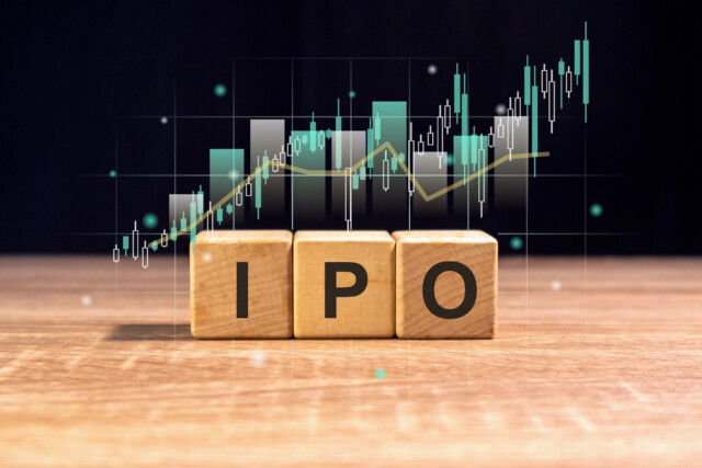 Three wooden blocks with the letters IPO are on a wooden surface. A digital stock chart with rising bars and lines is in the background, symbolizing Initial Public Offering and stock market growth.